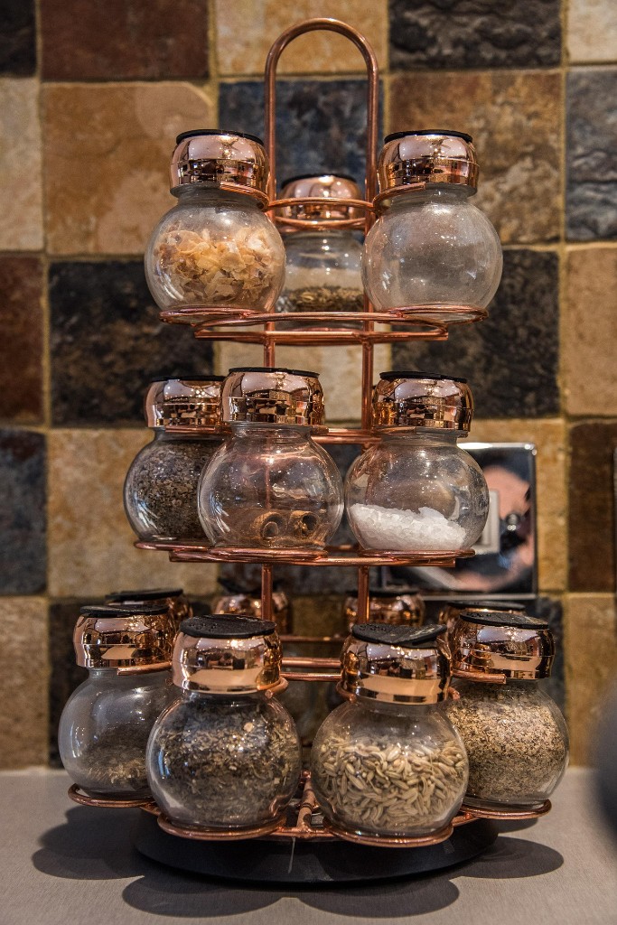 Copper spice rack filled with glass jars of herbs and spices on a kitchen counter